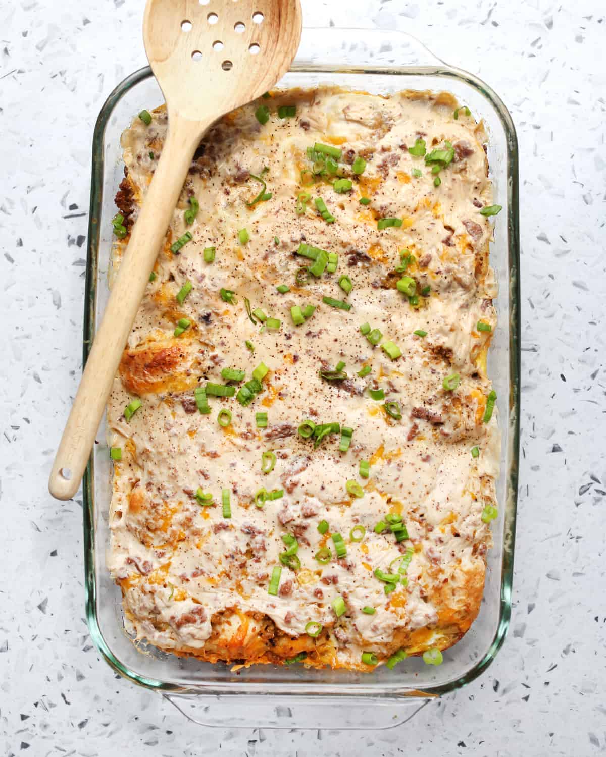 biscuits and gravy casserole in a glass pan with a wooden spoon on top